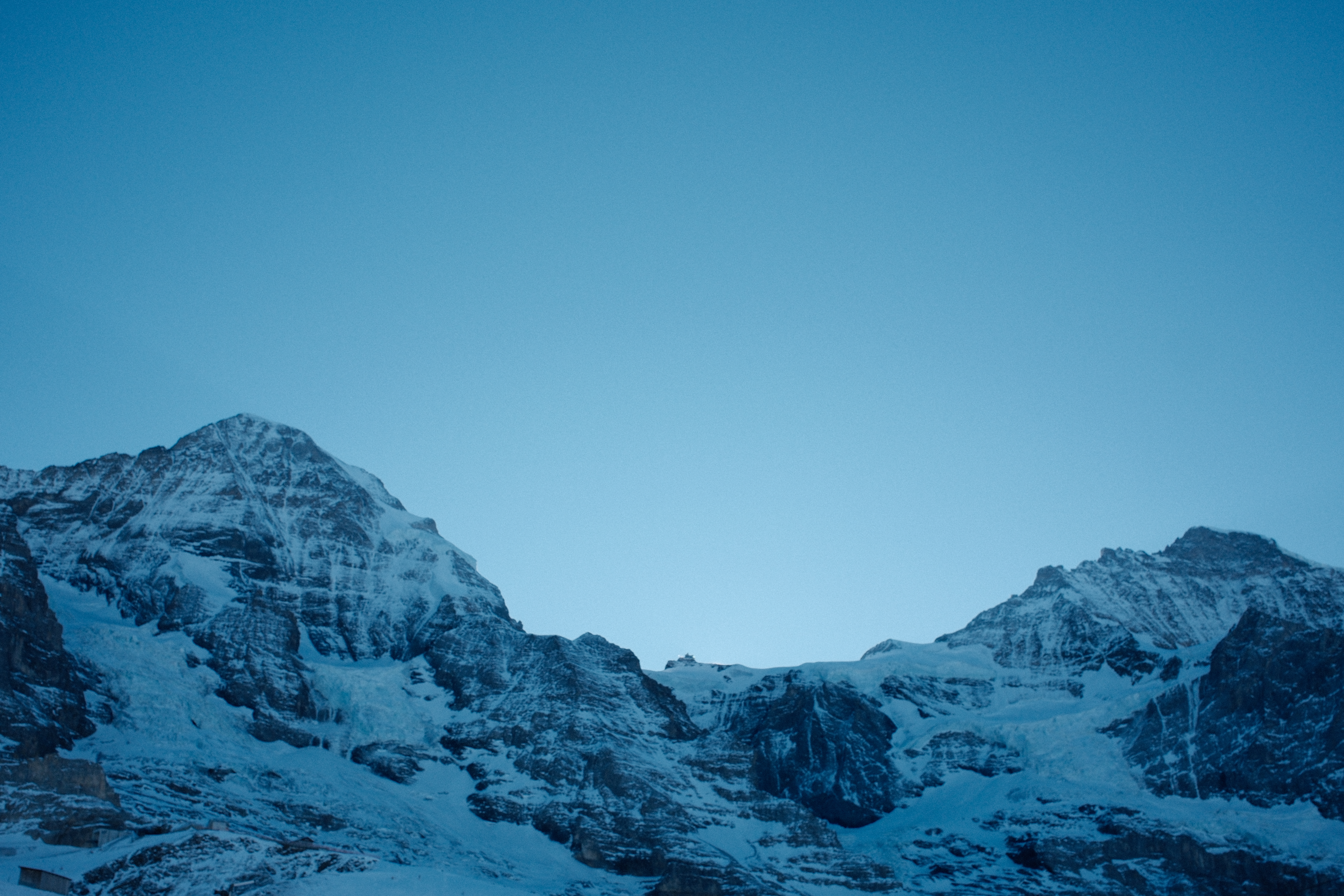 Snow-covered alpine peaks against a clear deep blue sky at dusk