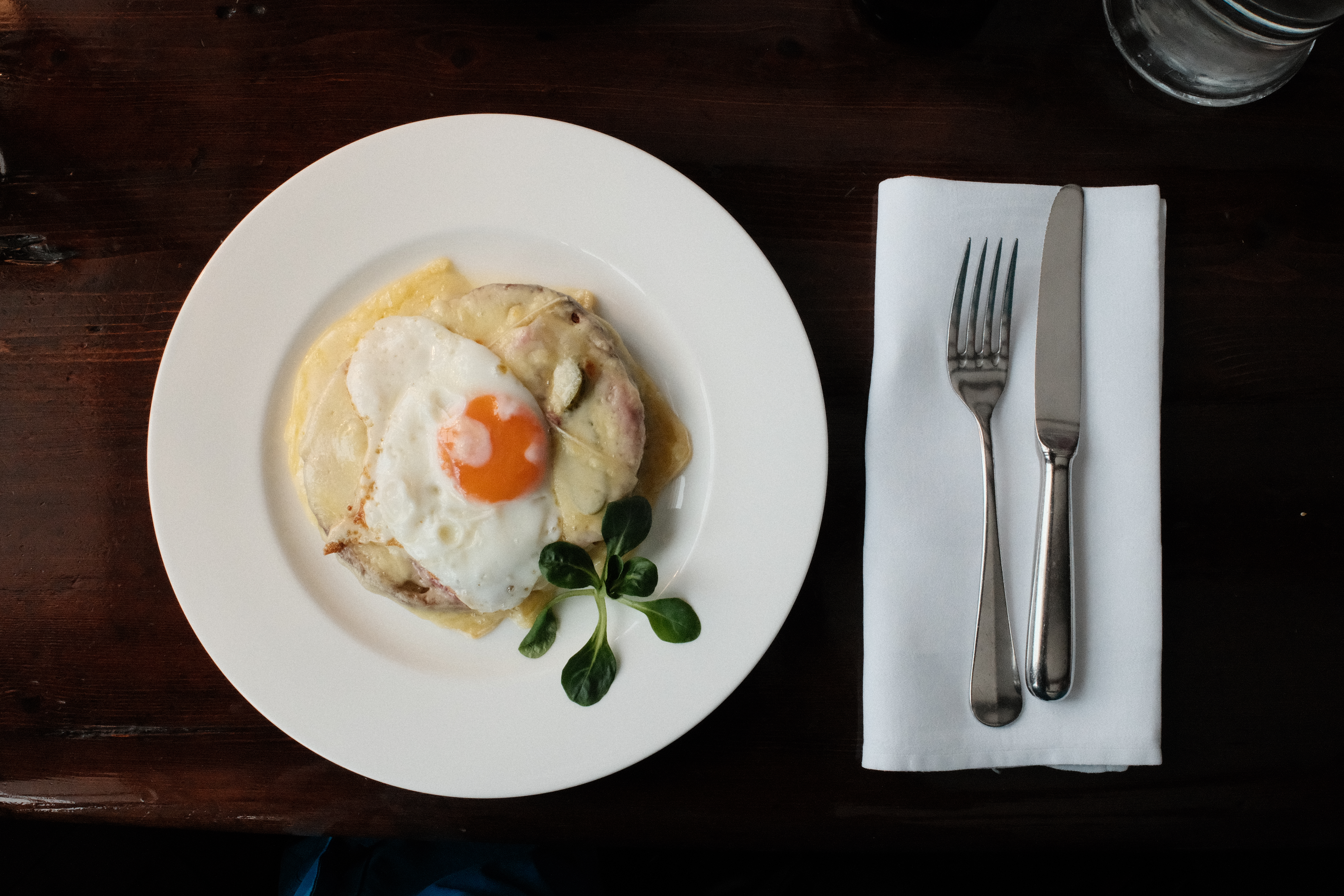 A fried egg on polenta on a white plate, cutlery and a white napkin alongside