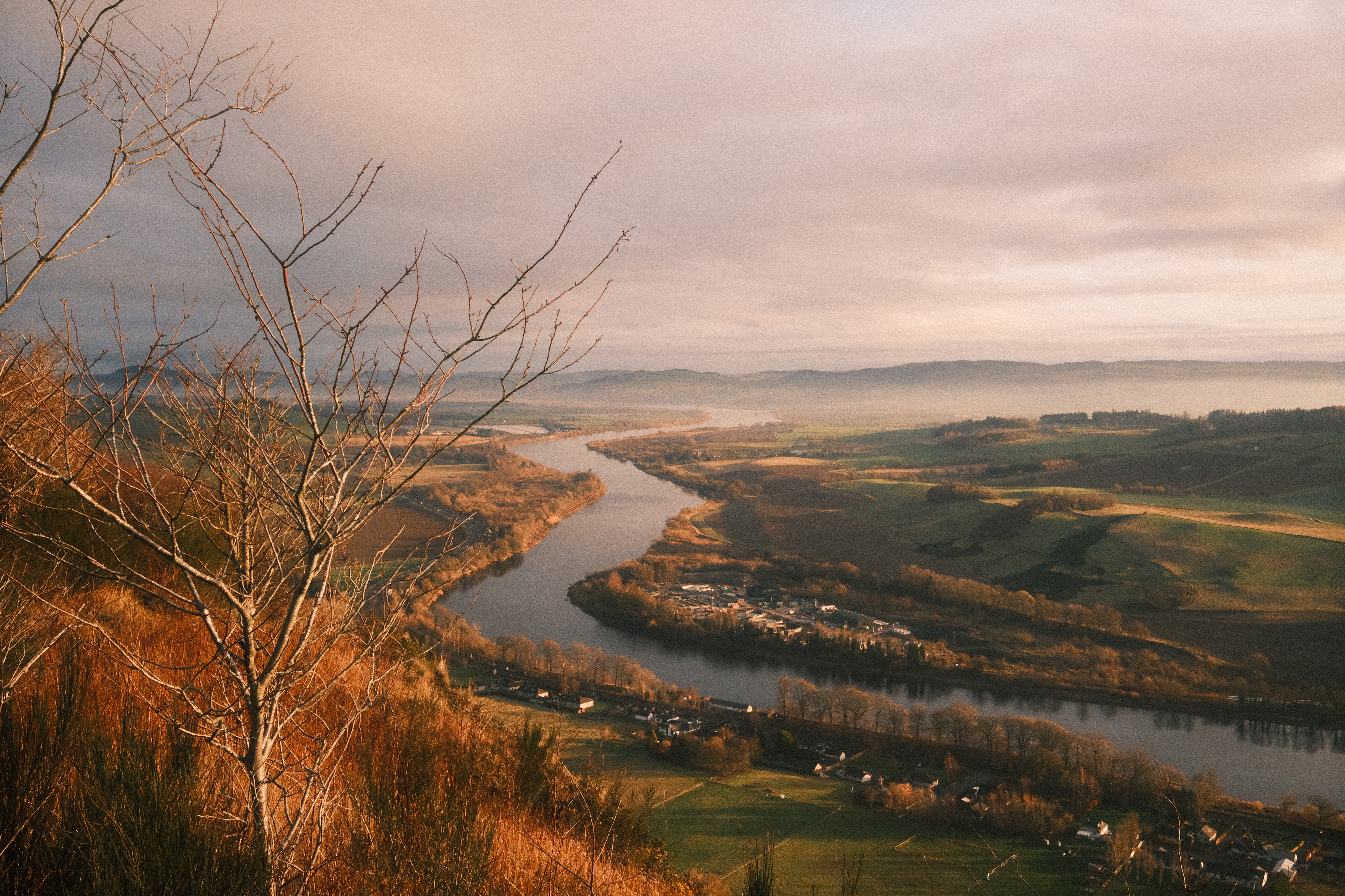 A winding river through a golden valley at sunrise, mist over distant hills