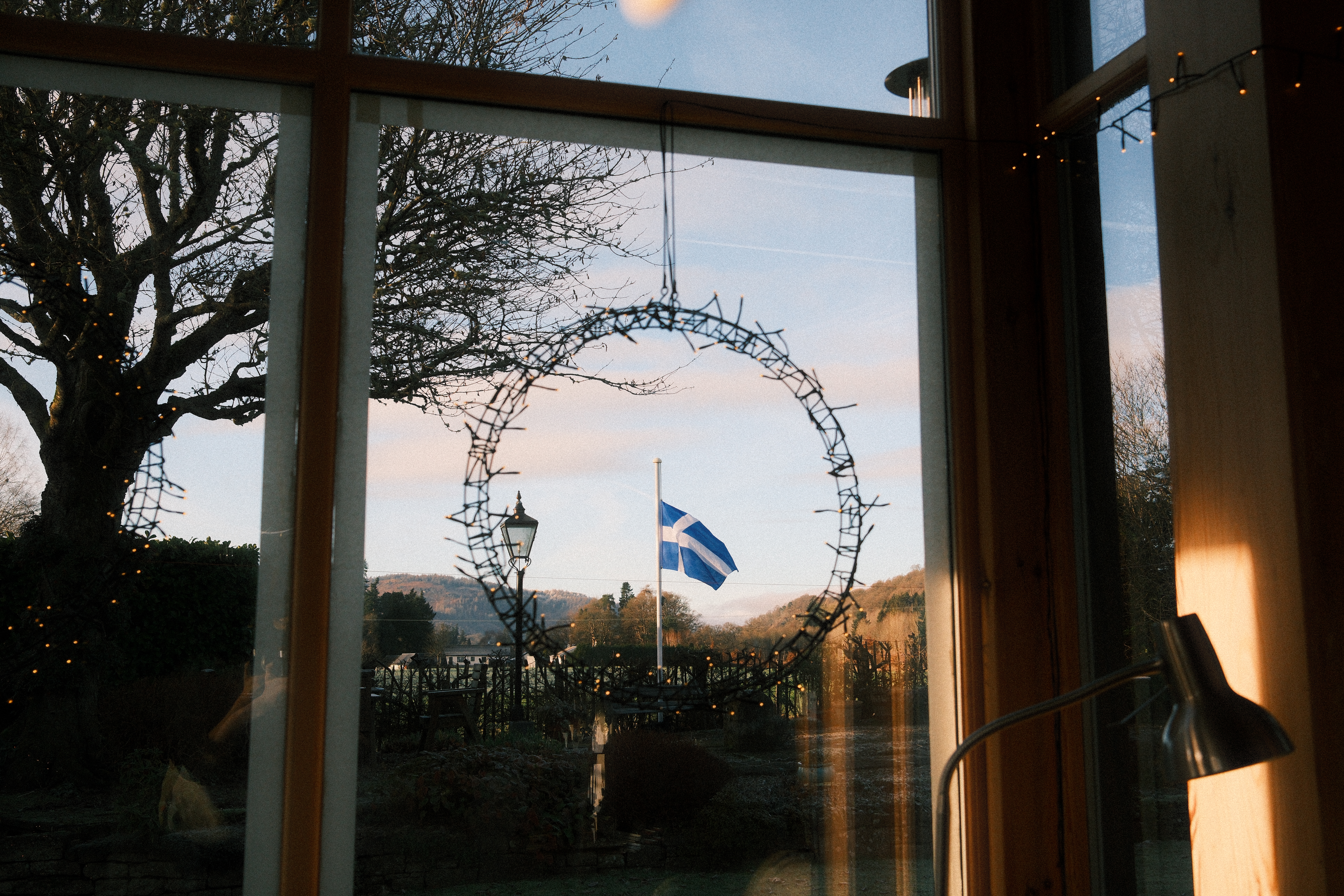 View through a window with a Shetland flag outside, hills and bare trees in the background