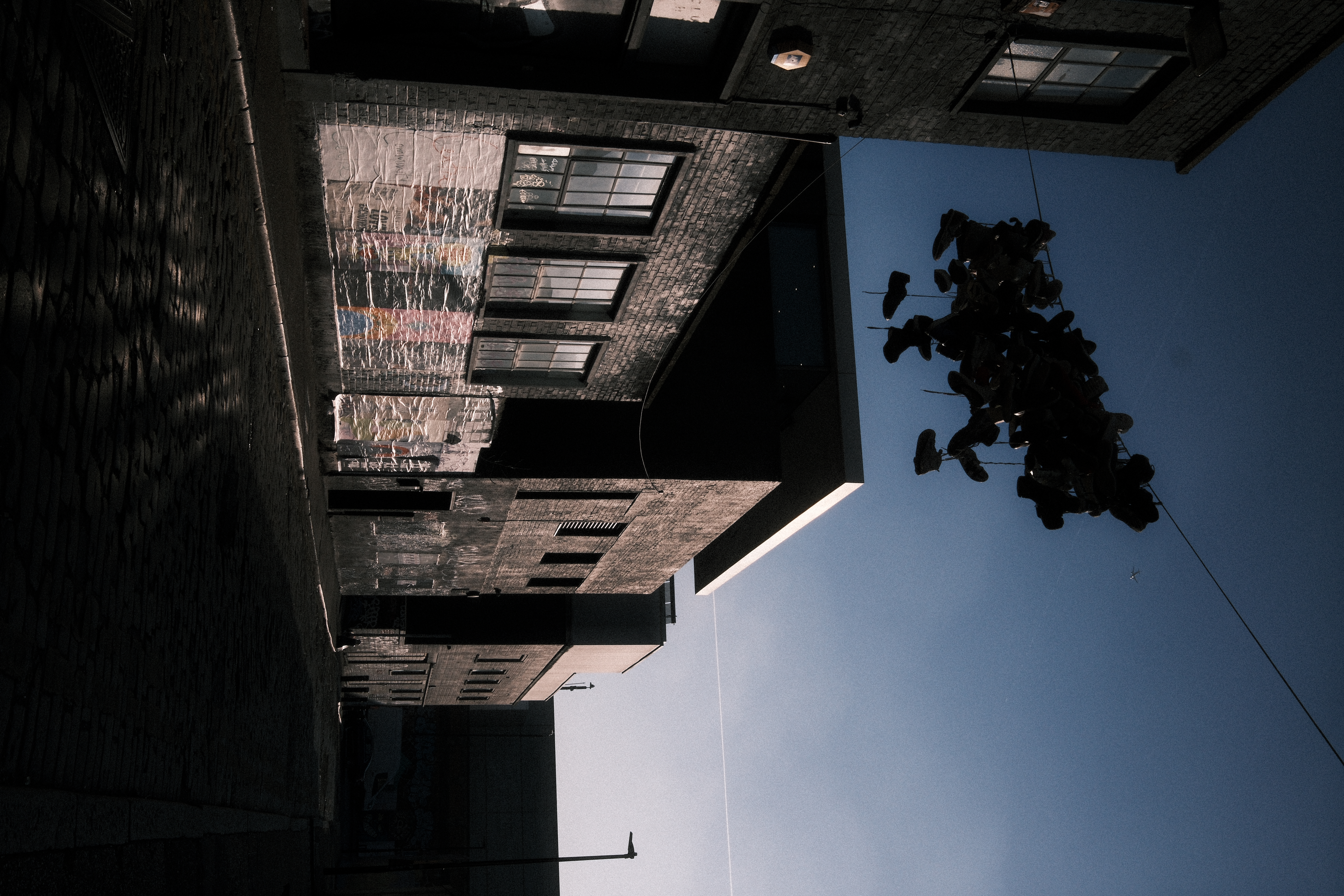 Shoes hanging from a wire above a cobbled back street between brick buildings