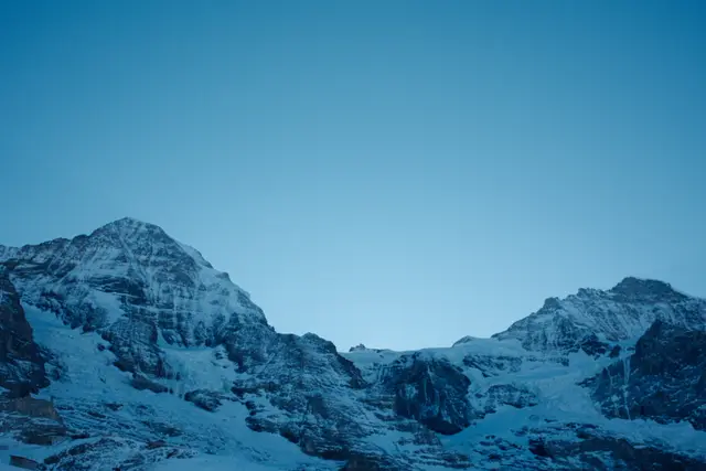 Snow-covered alpine peaks against a clear deep blue sky at dusk